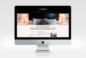 iMac screen displaying the home page of the Maretinborough Hotel website with hotel interior image of comfortable bed with lights either side and a black headboard